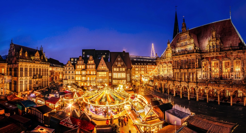 Eine historische Kulisse mit einem Weihnachtsmarkt, der in der Abendstimmung leuchtet.