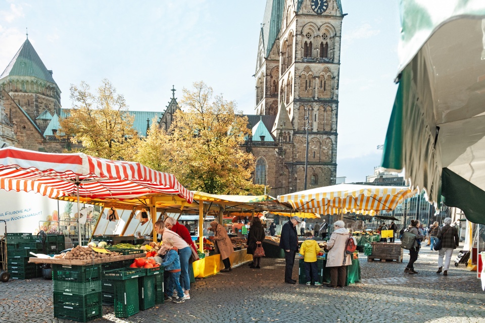 Menschen bummeln auf einem Wochenmarkt umringt von alten Gebäuden