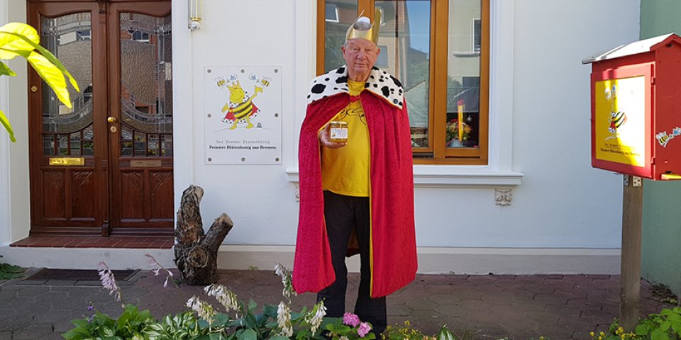 Heiner Lenz im Königskostüm und mit einem Glas Honig in der Hand vor seinem Haus in Walle.