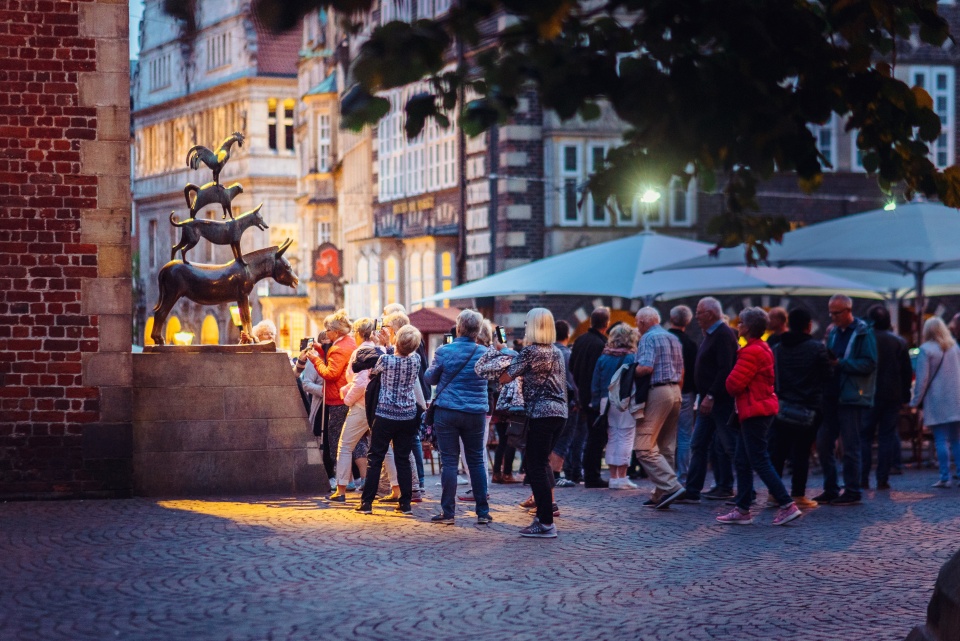 Die Aufnahme zeigt viele Menschen, die am Abend vor der Bronzestatue der Bremer Stadtmusikanten stehen und Bilder machen. 