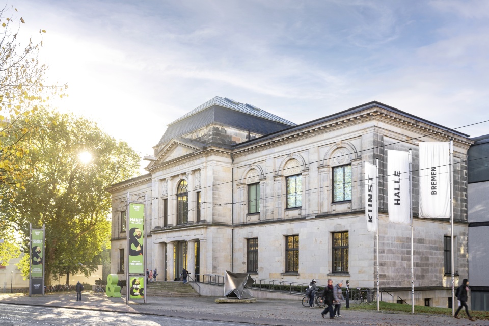 Außenansicht der Kunsthalle Bremen. Links neben dem Gebäude stehen Bäume, durch die die Sonne glitzert.