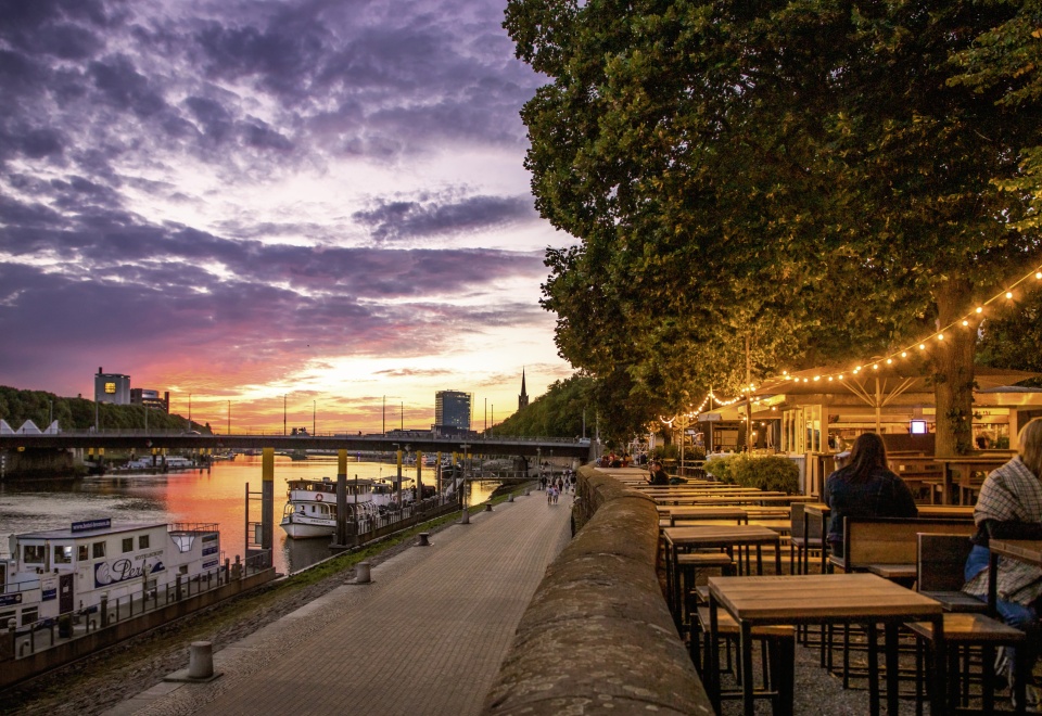 Die Flaniermeile "Schlachte" an der Weser bei Sonnenuntergang. Es befinden sich zahlreiche Schiffe auf dem Wasser. 