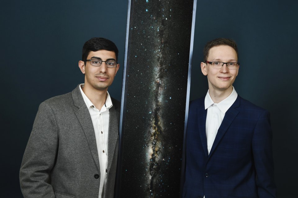 Zwei Jugendliche im Anzug vor dunklem Hintergrund und einem Bild der Milchstraße