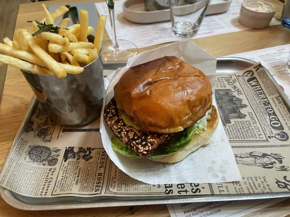 Ein Burger und Pommes liegen auf einem Tablett das mit Zeitungspapier ausgelegt ist.