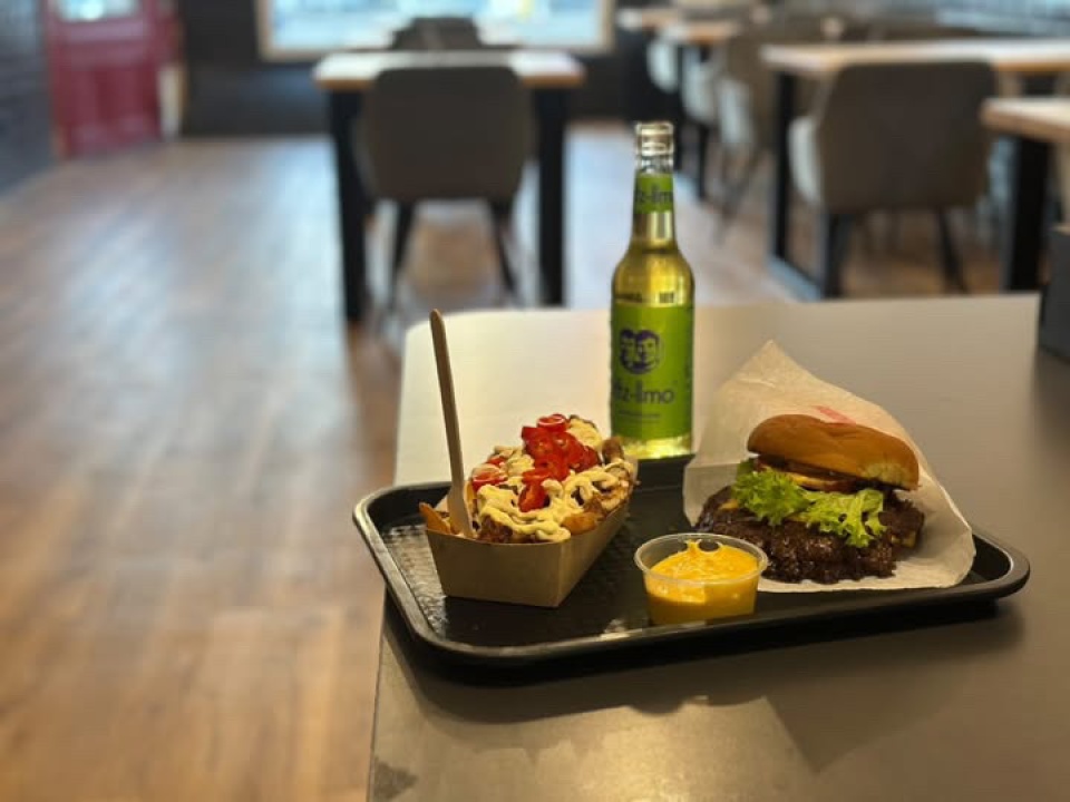 Tablett mit Burger, Pommes mit Soße und Getränk auf einem Tisch in einem Restaurant.
