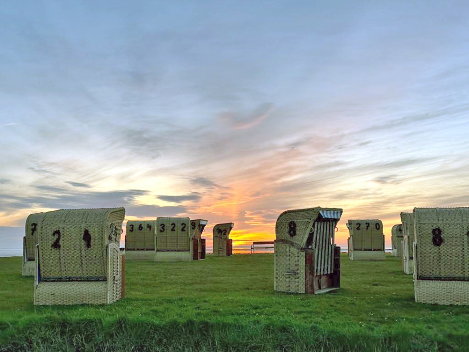 There are multiple beach chairs spread out with a sunset in the background.