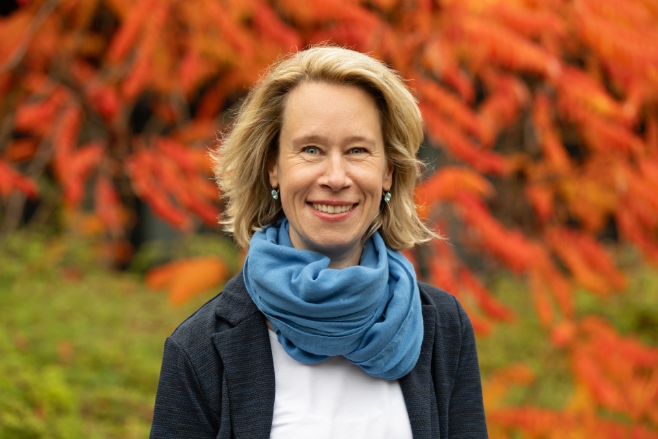 Eine Frau steht lachend vor einer Hecke in herbstlichen Farben