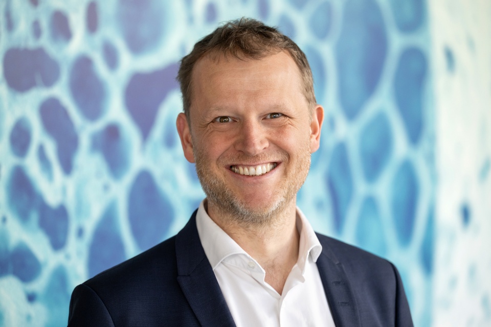 EIn Mann steht lachend vor einem blauen Hintergrund
