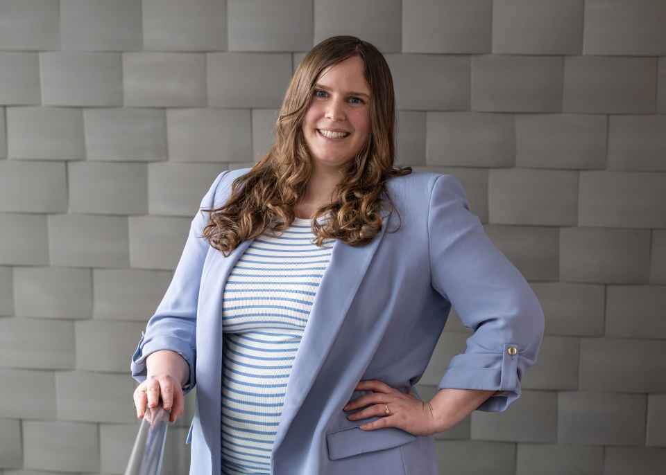 Eine junge Frau in einem hellblauem Blazer lacht freundlich.