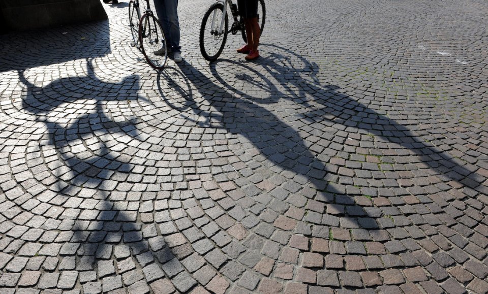 Zwei Personen schieben ihre Fahrräder an den Stadtmusikanten vorbei. Ihre Schatten sind zu sehen.