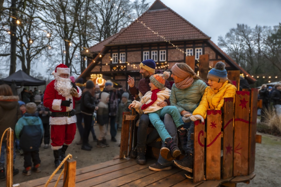 Eine Familie sitzt auf einem Weihnachtsmarkt. Daneben steht ein Weihnachtsmann.