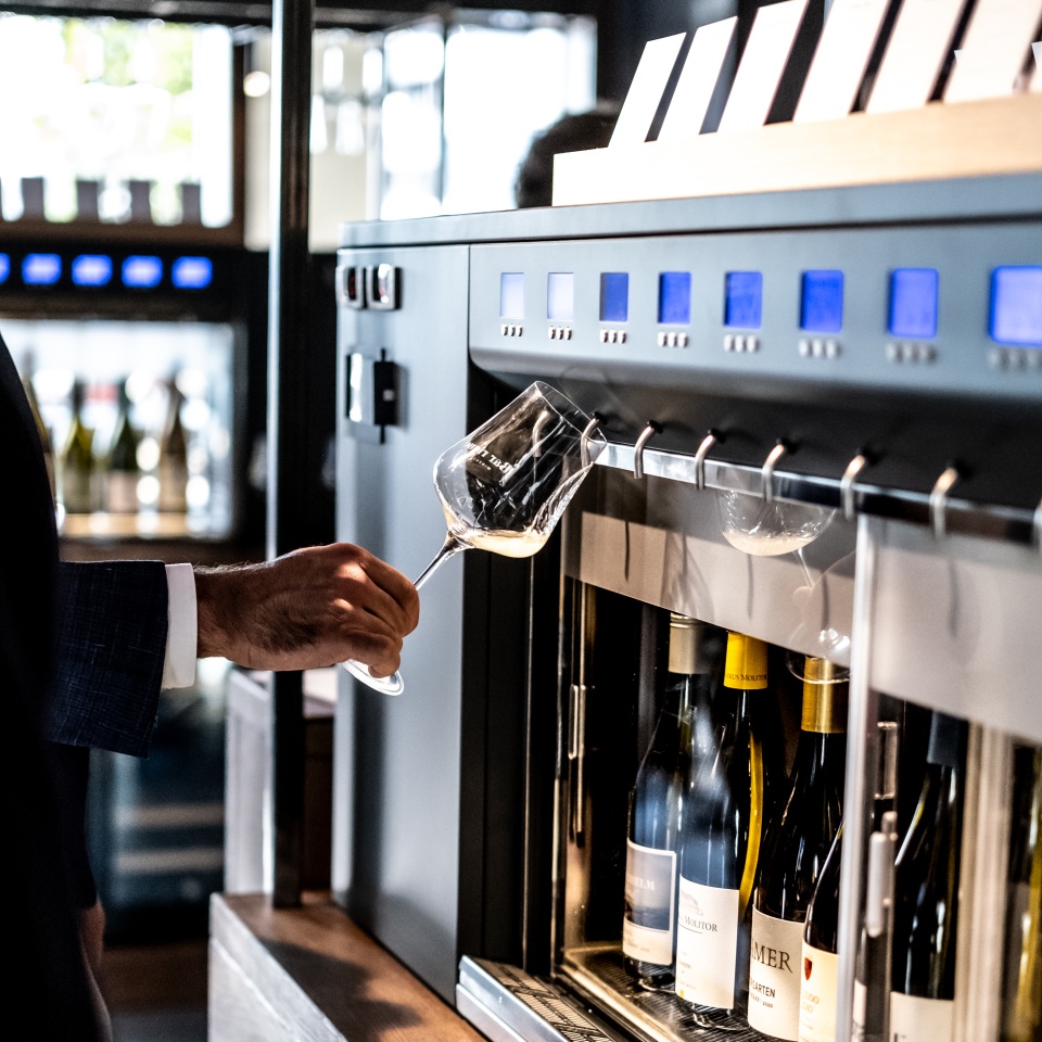 Eine Person zapft sich ein Glas Wein aus einem Weinautomaten