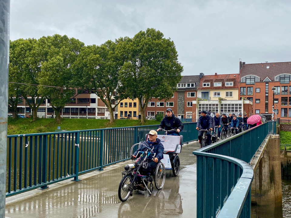 Die Teilnehmenden bei der Eröffnungsfahrt zur Handbike Tour. Sie fahren über eine Brücke. Vorne fährt ein Teilnehmer mit einem Handbike, dahinter ein "Pedder" Spezialrad, gefolgt von weiteren Personen mit Fahrrädern und Tandems.
