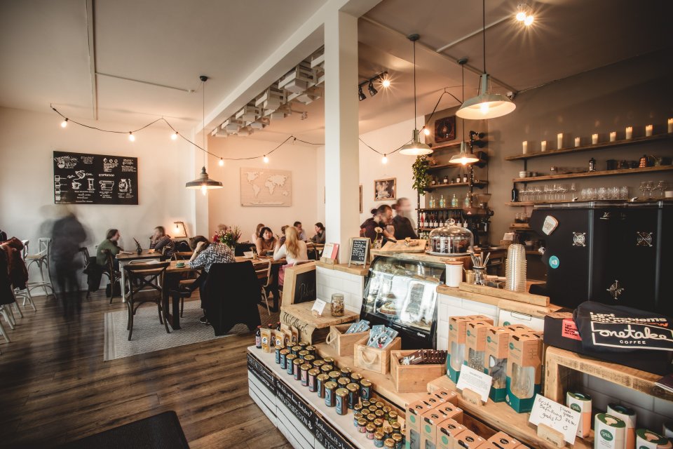 Das Café von innen. Auf Palletten sind verschiedene Kaffeesorten aufgestellt und es sitzen verschiedene Gäste im Café.