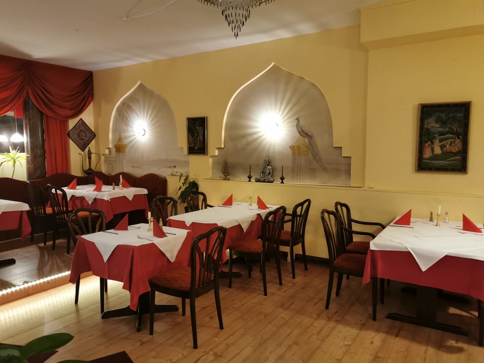 Das Restaurant von innen. Es stehen mehrere Tische und Stühle in einem gelben Raum. Die Beleuchtung von den Wänden erhellt den Raum.