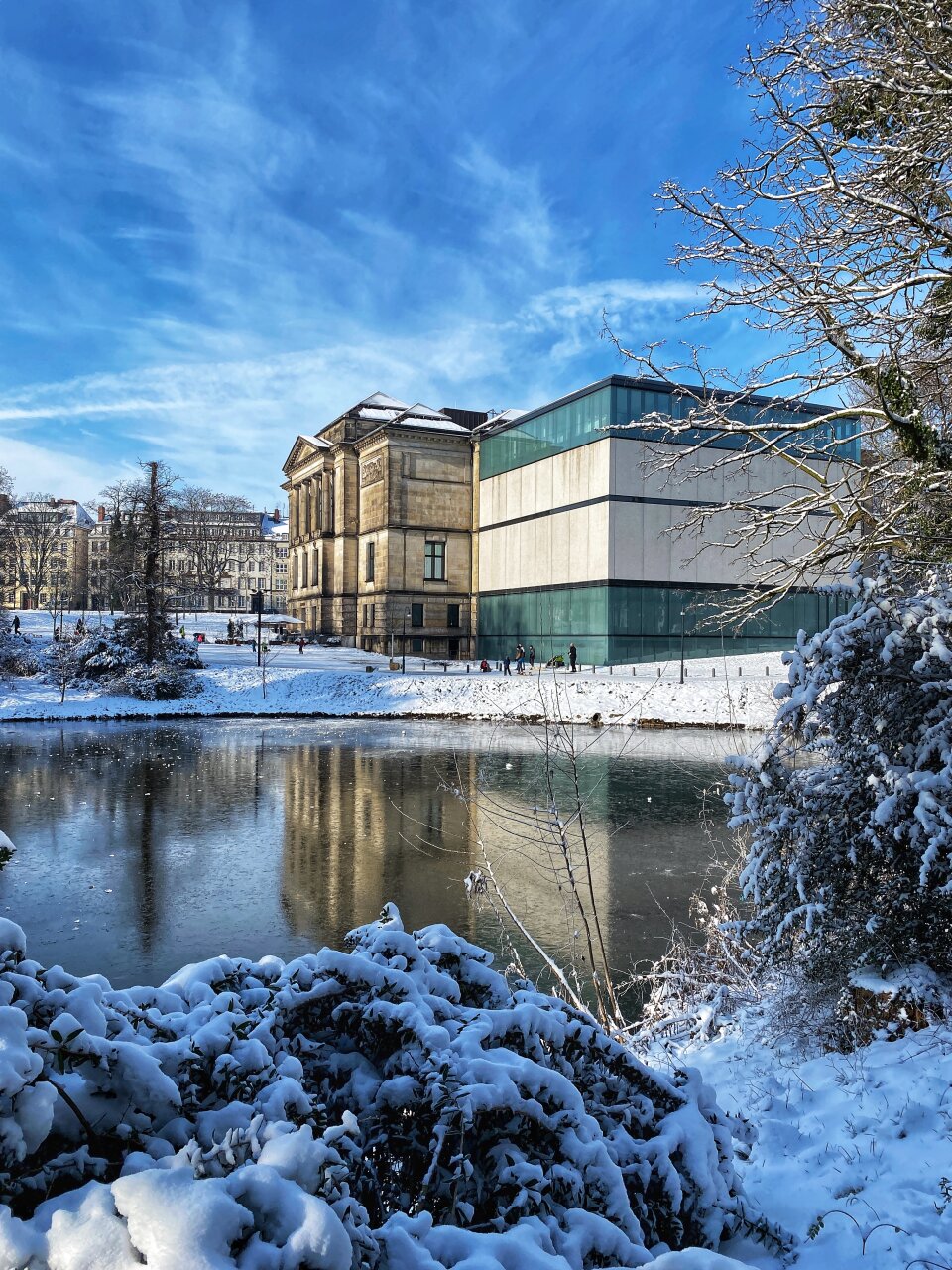 Dunsthalle spiegelt sich in einem kleinen See. Die Landschaft drumherum ist in Schnee gehüllt und Kinder spielen darin.