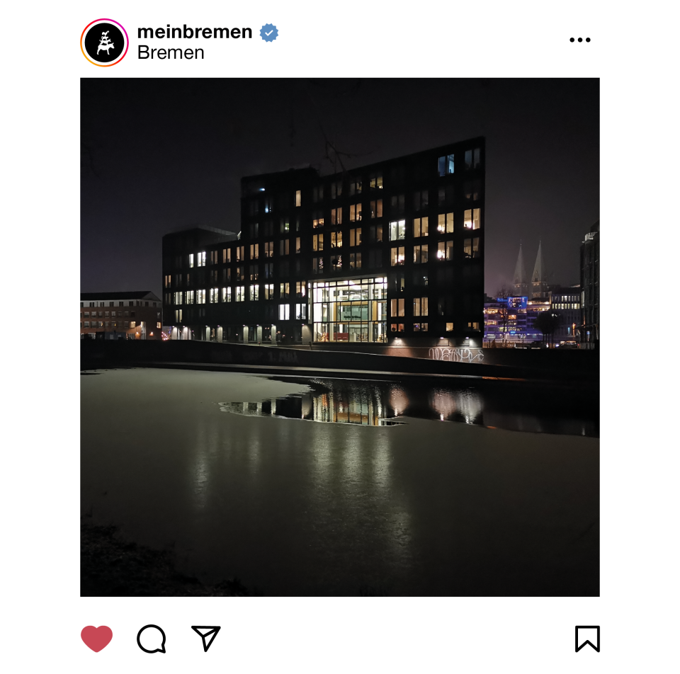 Ein Gebäude wird in der Dunkelheit beleuchtet. Davor ist ein Fluss zu sehen.