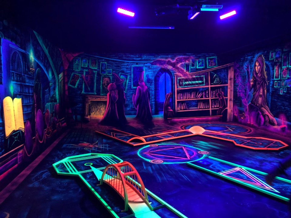 Ein Raum der Minigolf Helden in Findorff. Die Wände sind in bunter Neonfarbe bemalt. Es sind Hexen und Zauberer zu sehen. 