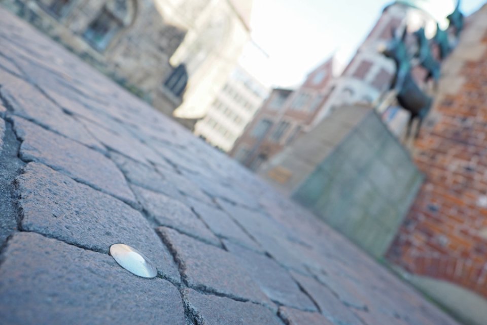 Ein Nagel im Boden steht im Fokus, im Hintergrund sieht man verschwommen die Bremer Stadtmusikanten.