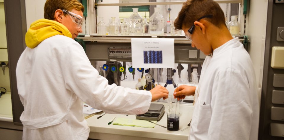 Zwei Jungen im Schutzanzug nehmen eine Probe in einem Chemielabor