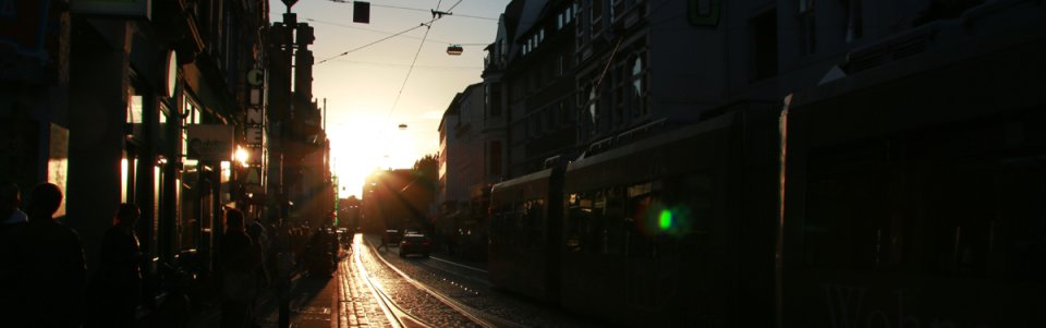 Die Sonne steht tief über dem Steintor mit Passanten und Straßenbahn.