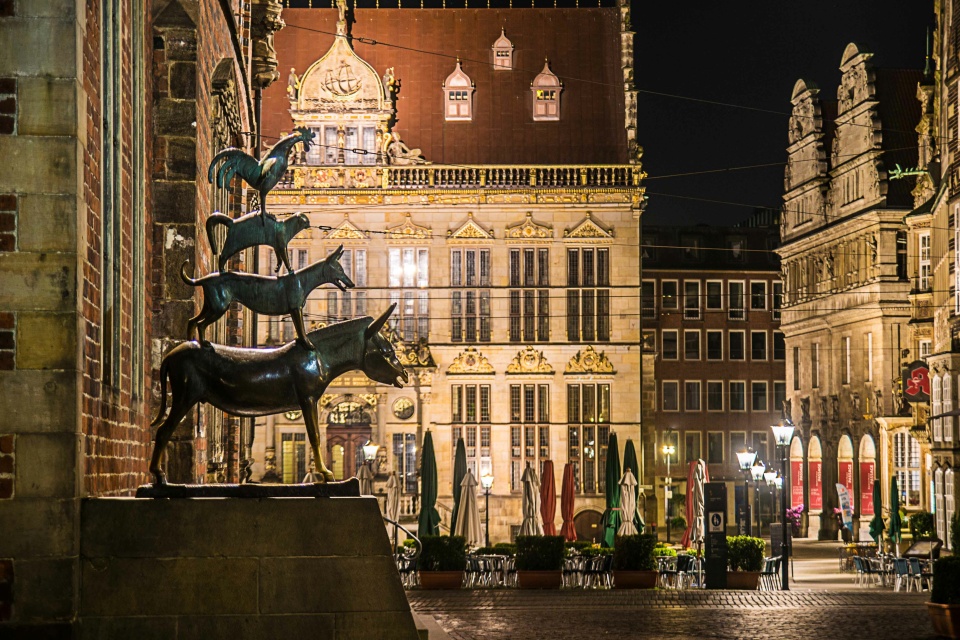 Blick auf die Bremer Stadtmusikanten bei Nacht vor dem Hintergrund des beleuchteten Marktplatzes mit dem Schütting.