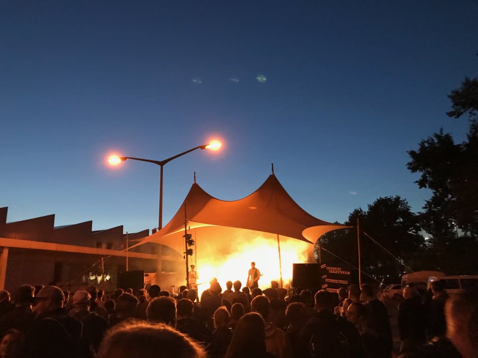 Eine Band spielt im Abendlicht vor vielen Menschen auf einer Bühne. 