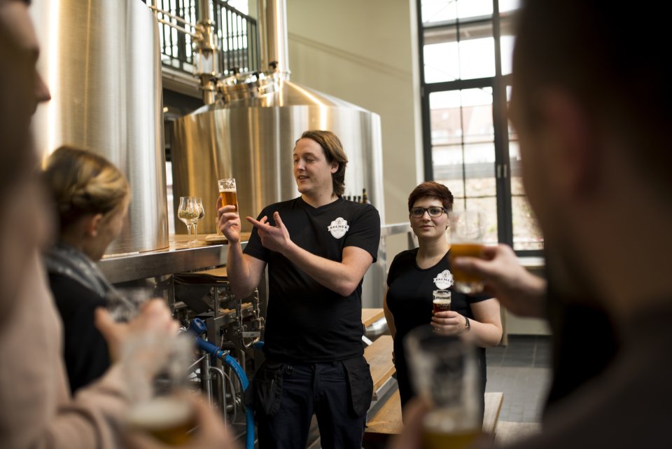 Ein Mitarbeiter und eine Mitarbeiterin der Union Brauerei führen eine Brauereiführung für Gäste durch.