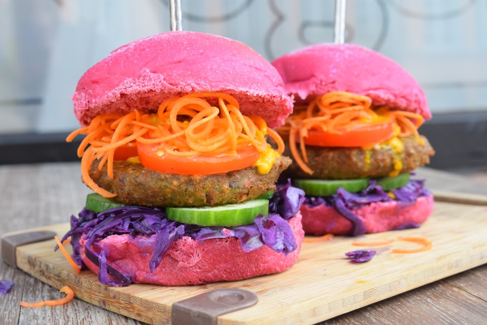 Eine Großaufnahme von einem veganen Burger. Das Brötchen ist rosa.