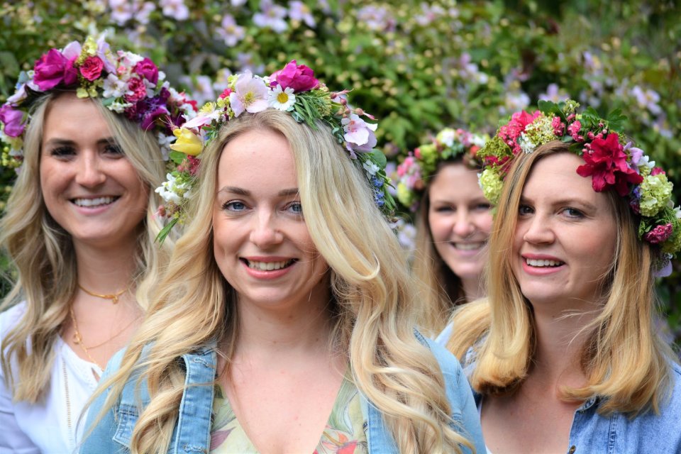 Vier Frauen mit einem Blumenkranz auf dem Kopf lachen in die Kamera. 